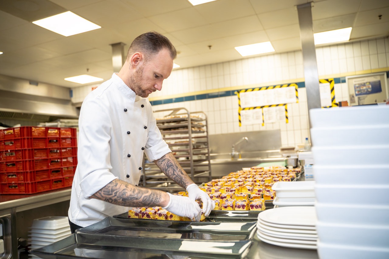 Ein Koch des Holiday Inn Munich City Centre arbeitet in der Küche und richtet Kuchen auf Tabletts.